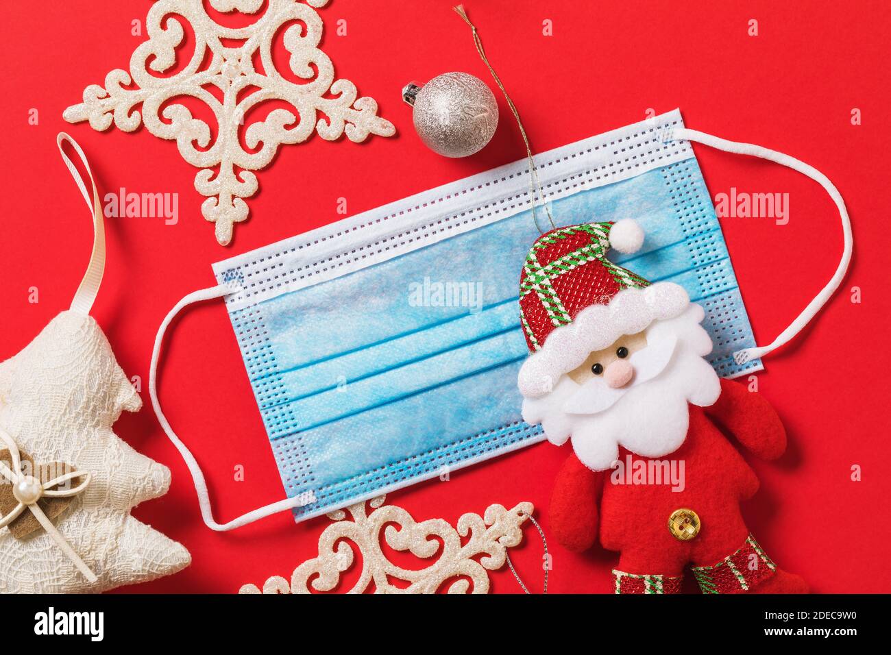 Weihnachtsschmuck und eine medizinische Maske auf rotem Hintergrund, Draufsicht. Urlaub Quarantänekonzept aufgrund covid-19 Pandemie. Stockfoto