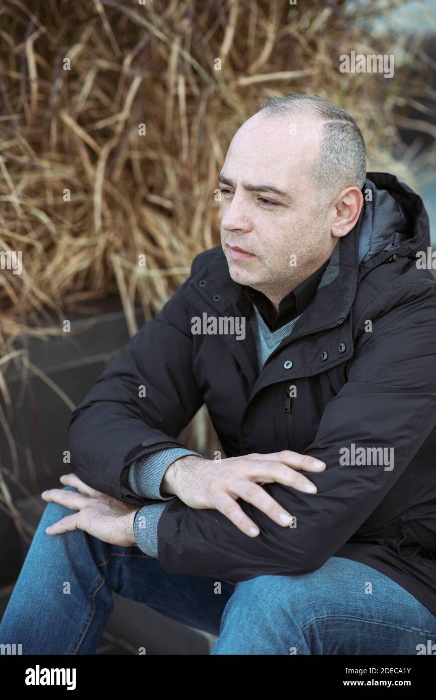 45 Jahre alter Mann, der draußen sitzt Stockfoto