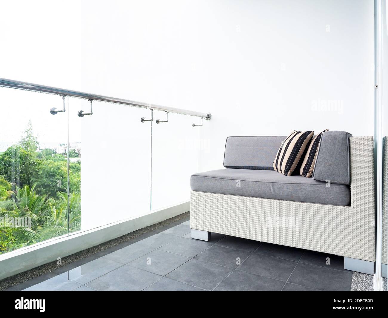 Komfortables Rattan-Sofabett mit Kissen auf dem Balkon und Terrasse auf einem hohen Gebäude mit weißem Hintergrund in der Nähe von Glas Partition außerhalb des Stockfoto