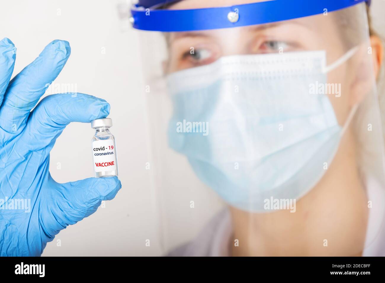 Arzt mit blauen Handschuhen und Visier hält ein Fläschchen mit Impfstoff oder Medikament auf weißem Hintergrund. Impfkonzept. Stockfoto