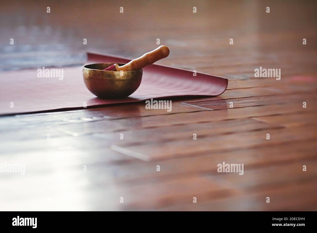 Eine Klangschale steht auf einer Yogamatte auf einem Holzboden mit Kopierfläche. Stockfoto