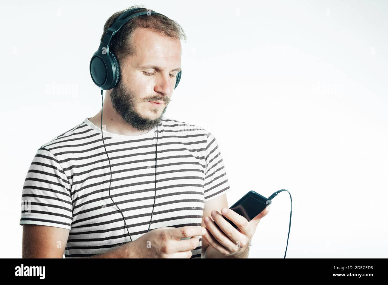 Ein bärtiger Mann hört Musik auf einem Smartphone mit großen Kopfhörern. 30-35 Jahre alt. Isoliert auf Weiß Stockfoto