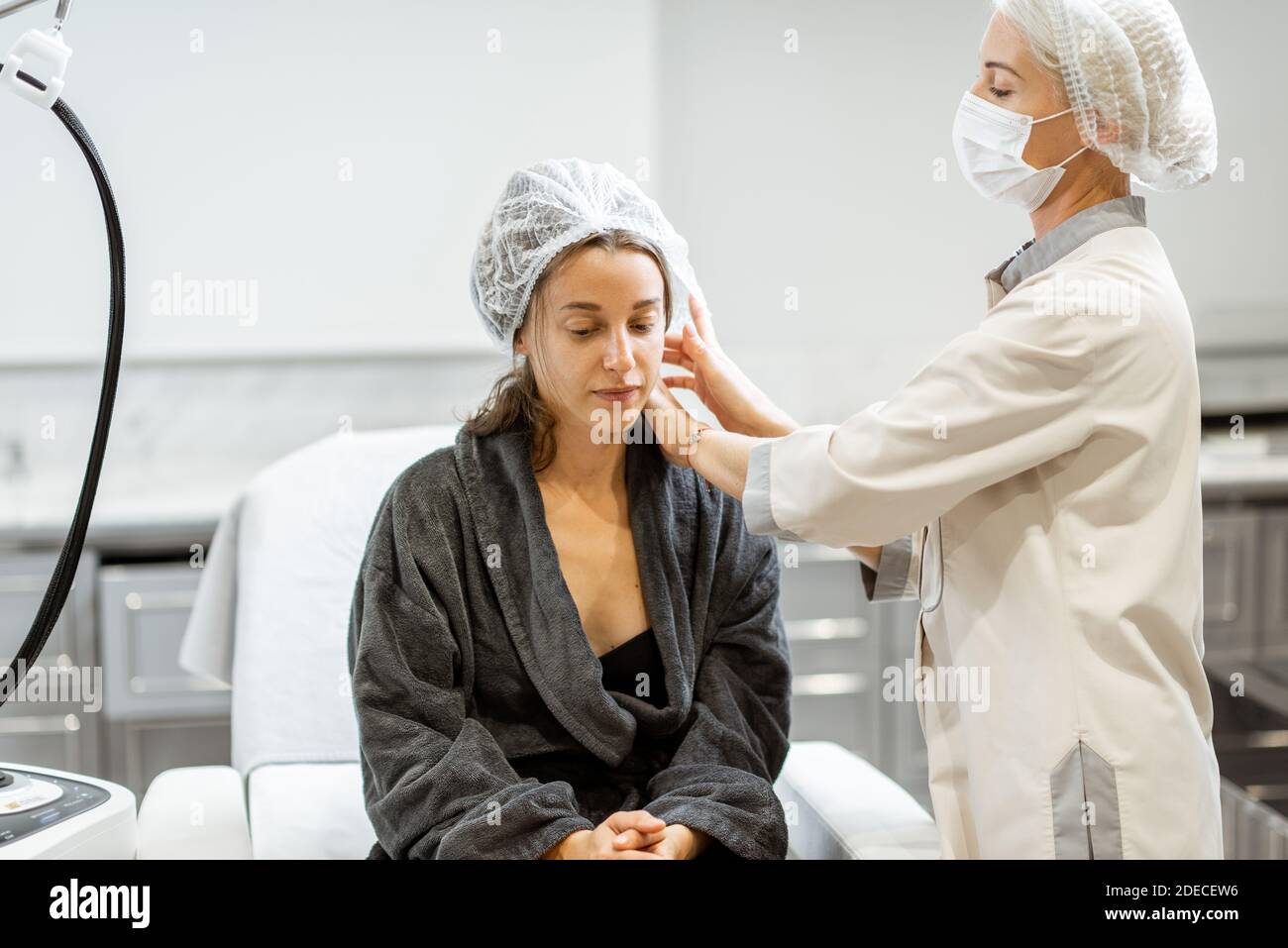 Junge Frau, die sich auf eine Verjüngungskur vorbereitet, trägt Schutzhut im medizinischen SPA-Büro mit einem Arzt Stockfoto