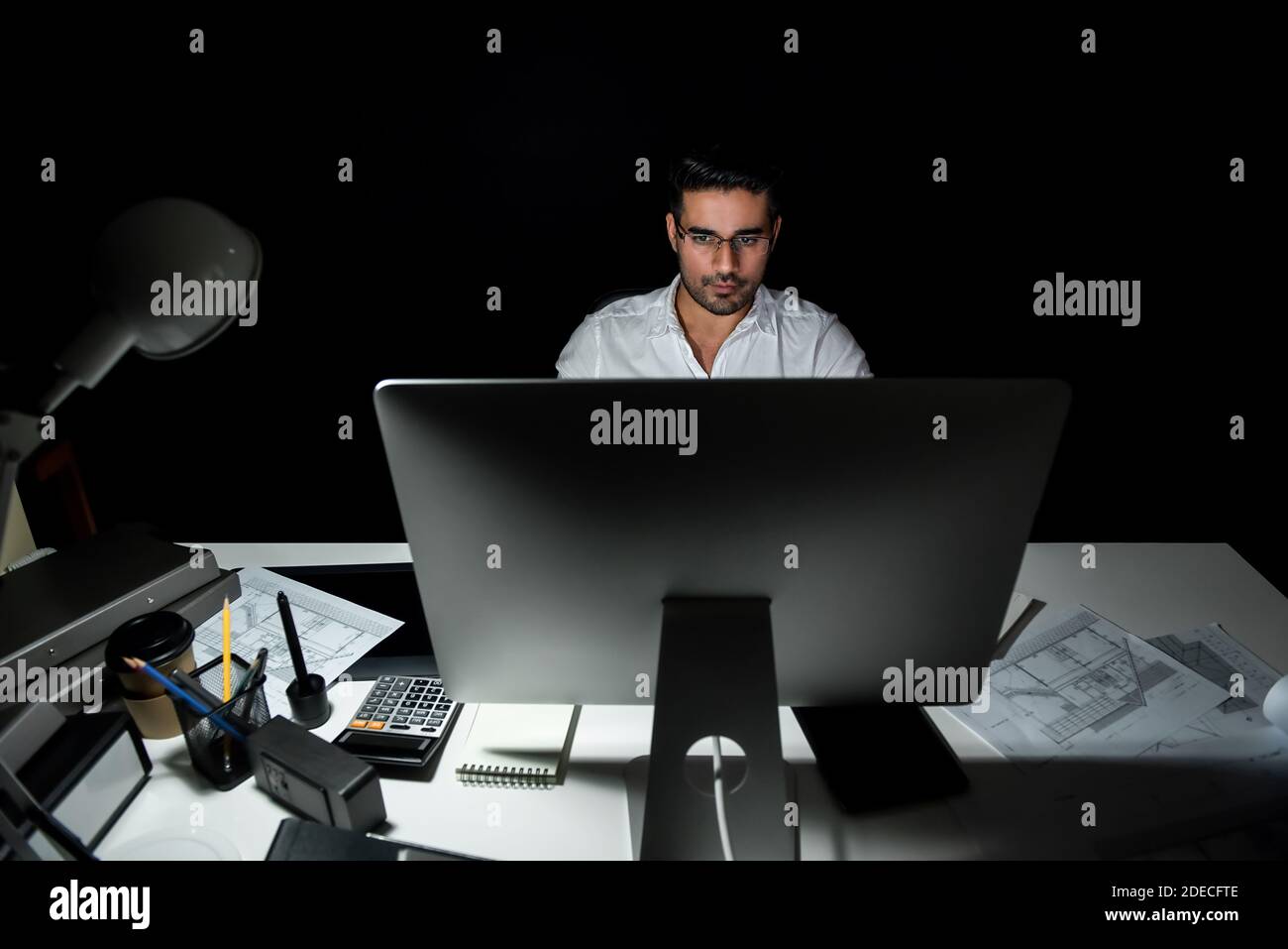 Engagierter asiatischer Architekt, der sich auf die Arbeit vor dem Computer konzentriert An seinem Schreibtisch spät in der Nacht im Büro Stockfoto