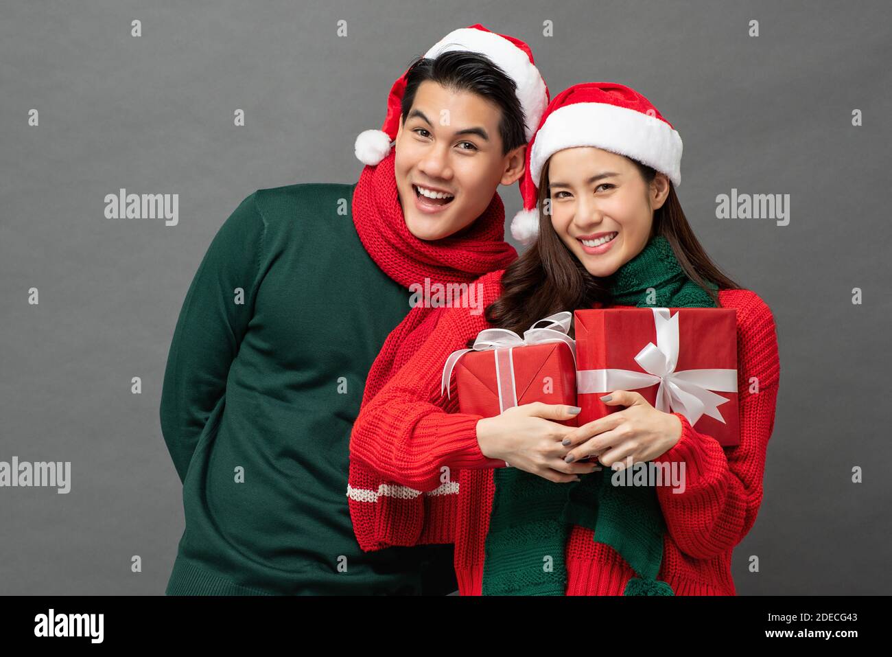 Glücklich lächelnd junge asiatische Paar trägt bunte rot und grün Pullover mit Weihnachts-Geschenkboxen Studio auf grauem Hintergrund aufgenommen Stockfoto