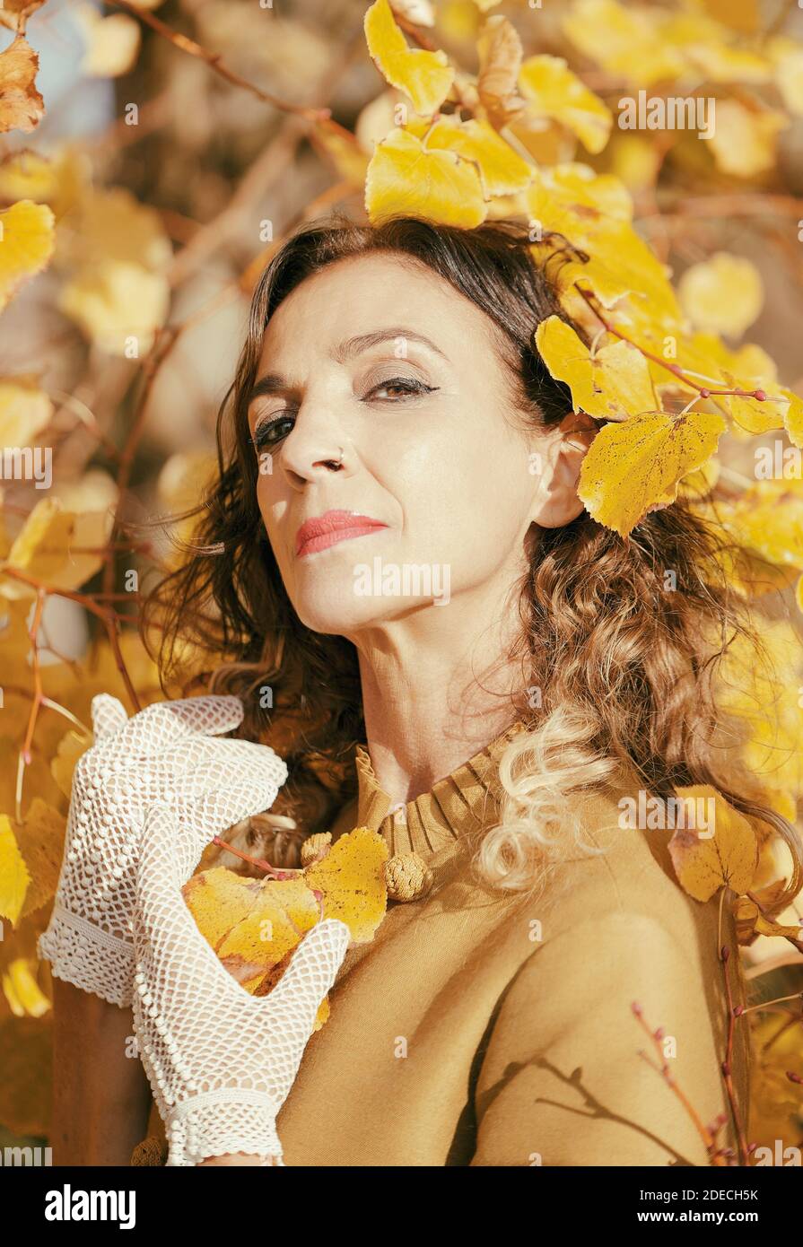 Frau mit Häkelhandschuhen zwischen den Zweigen eines goldenen Baum im Herbst Stockfoto