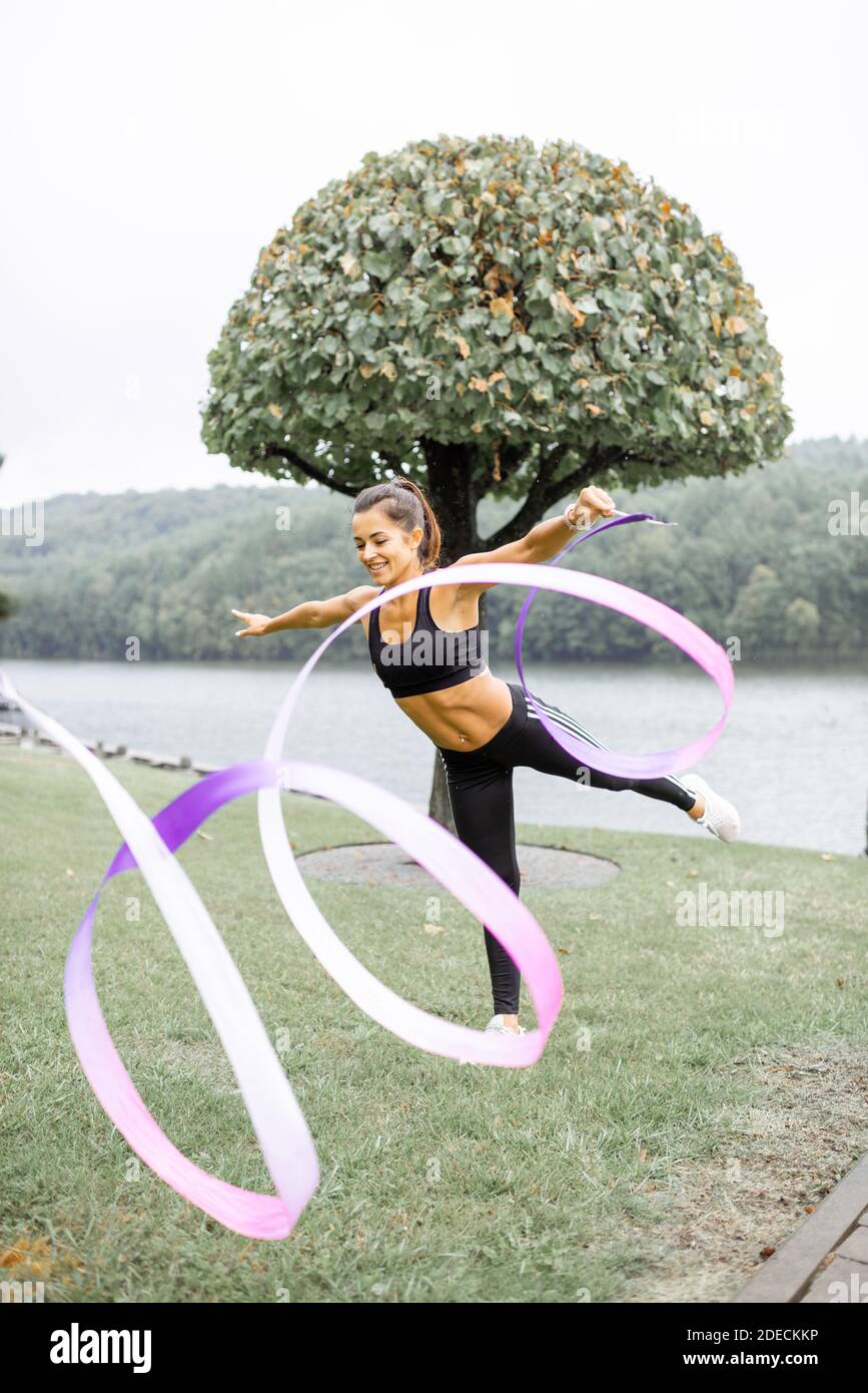 Athletische Frau, die rhythmische Gymnastik mit einem Band im Freien übt Stockfoto
