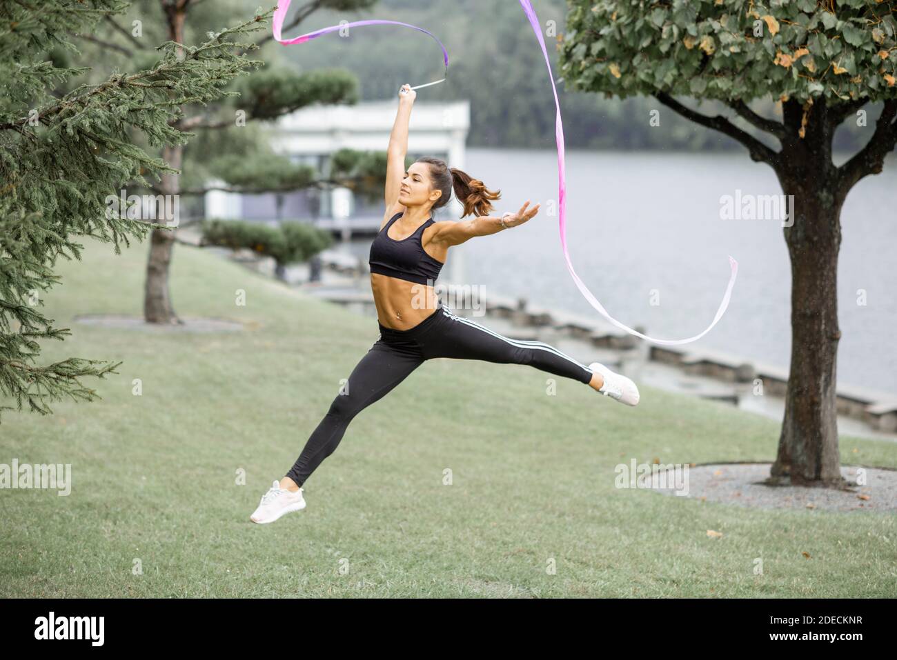 Athletische Frau, die rhythmische Gymnastik mit einem Band im Freien übt Stockfoto