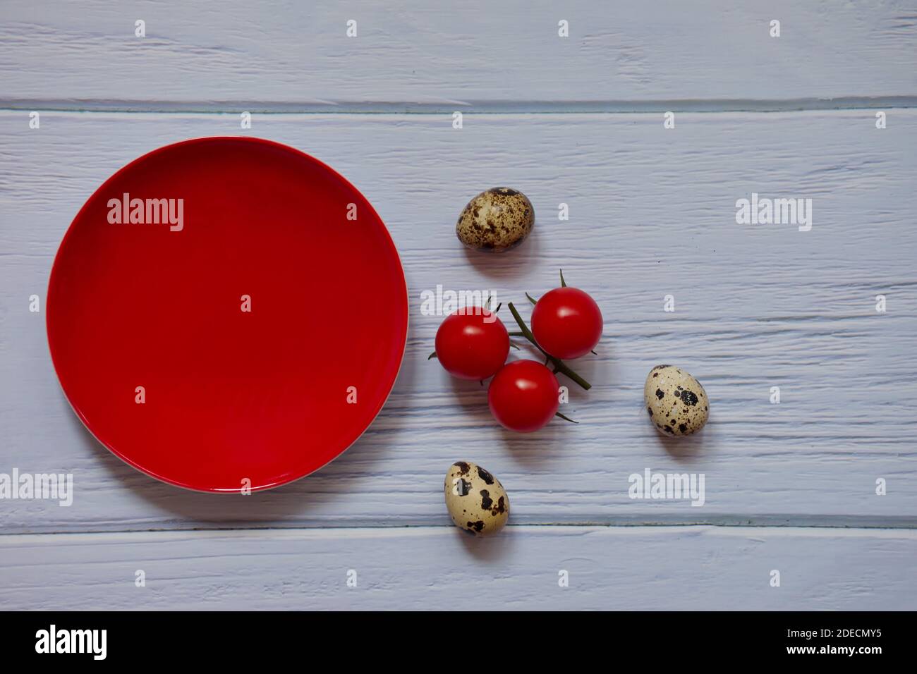Roter Teller, Kirschtomate und Wachteleier auf Holzhintergrund Stockfoto