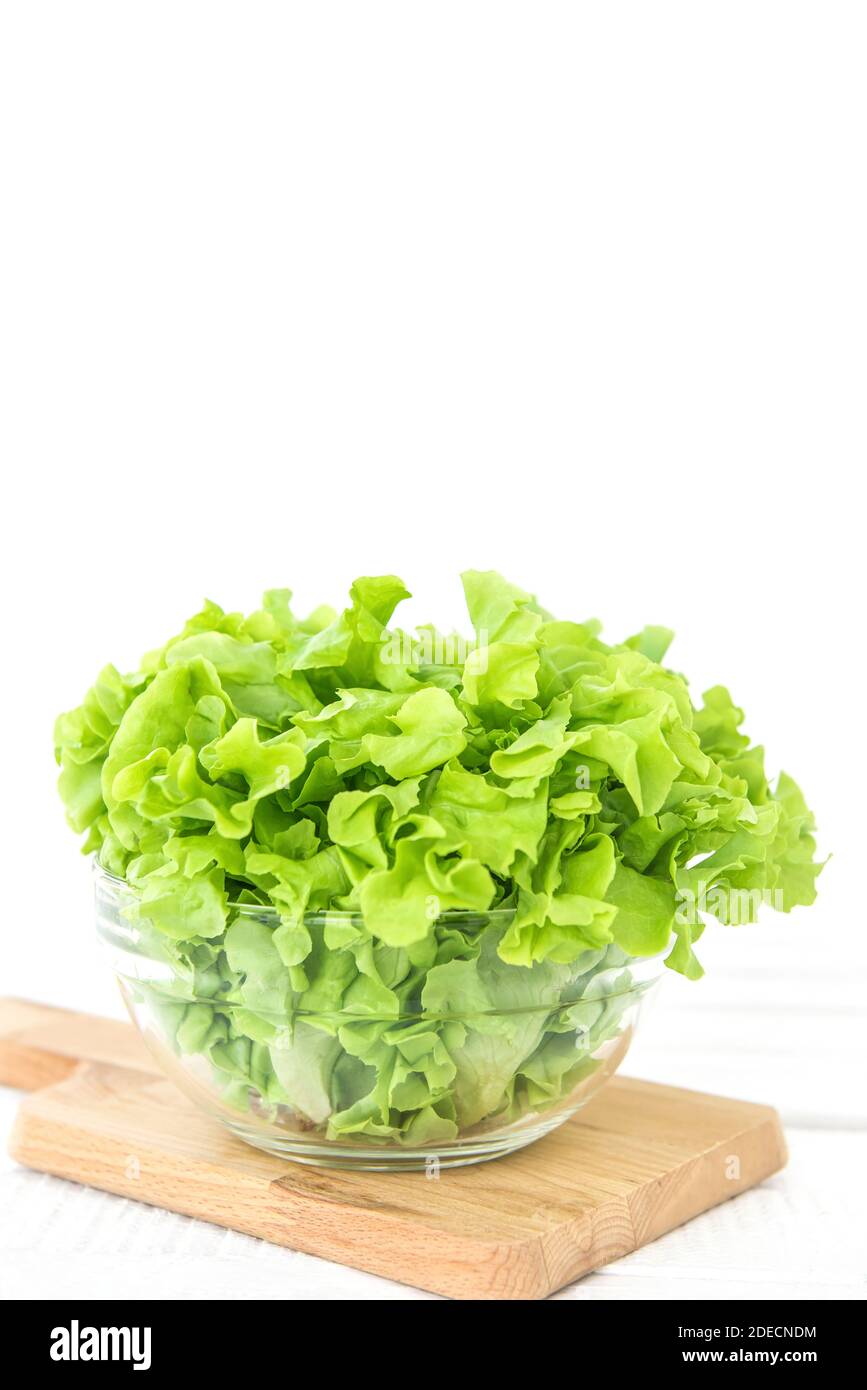 Frisches Gemüse, grüne Eichenblätter, in Glasschale auf Holzabtrennplatte gegen weißen Tischhintergrund, Seitenansicht Stockfoto