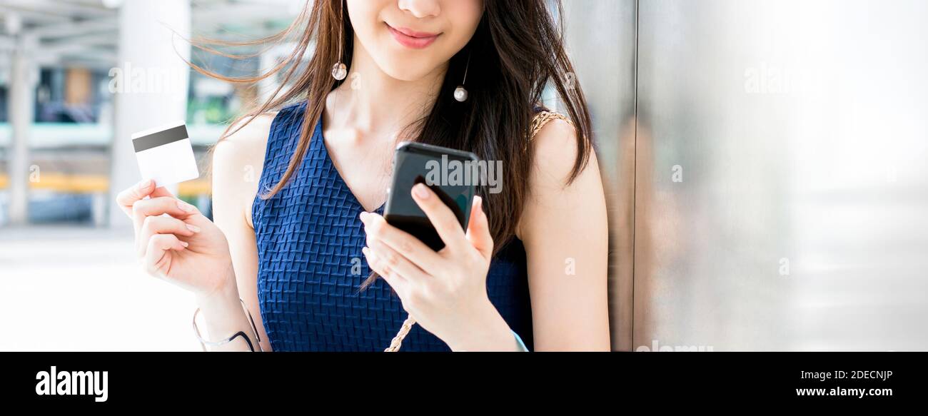 Junge lächelnde asiatische Frau, die Zahlung digital mit Kreditkarte nach dem Online-Shopping mit Handy-Anwendung, Panorama-Banner Stockfoto