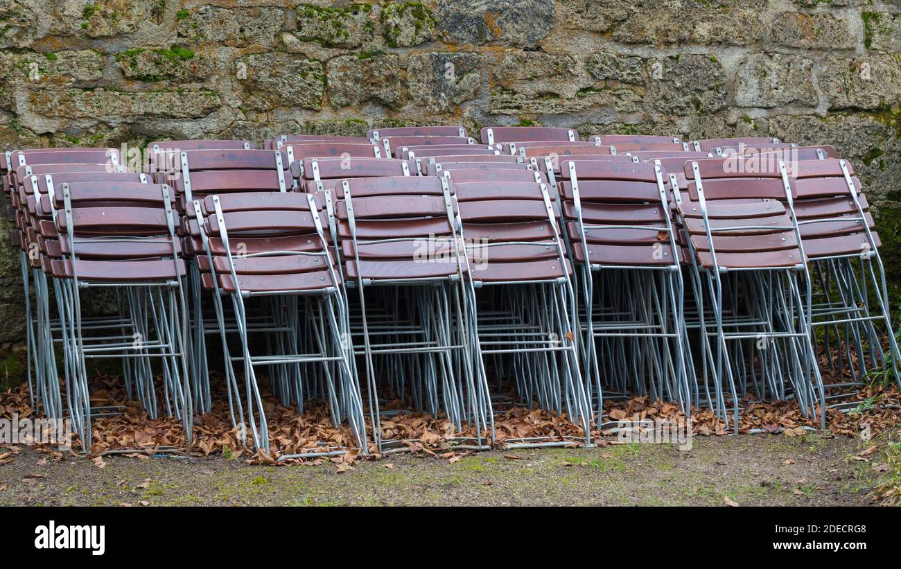 München, Bayern / Deutschland - 12. Nov 2020: Gefaltete Stühle lehnen sich an eine Steinwand. Alle Restaurants sind wegen der Covid-19-Sperre geschlossen. Stockfoto