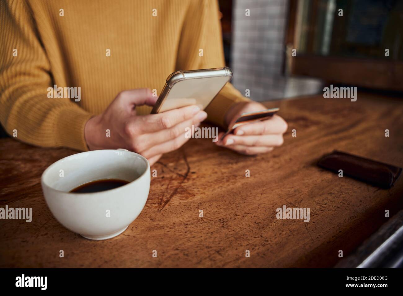 Nahaufnahme von jungen weiblichen Händen mit Smartphone und Bankkarte Während der Online-Zahlung im Café trinken Kaffee Stockfoto