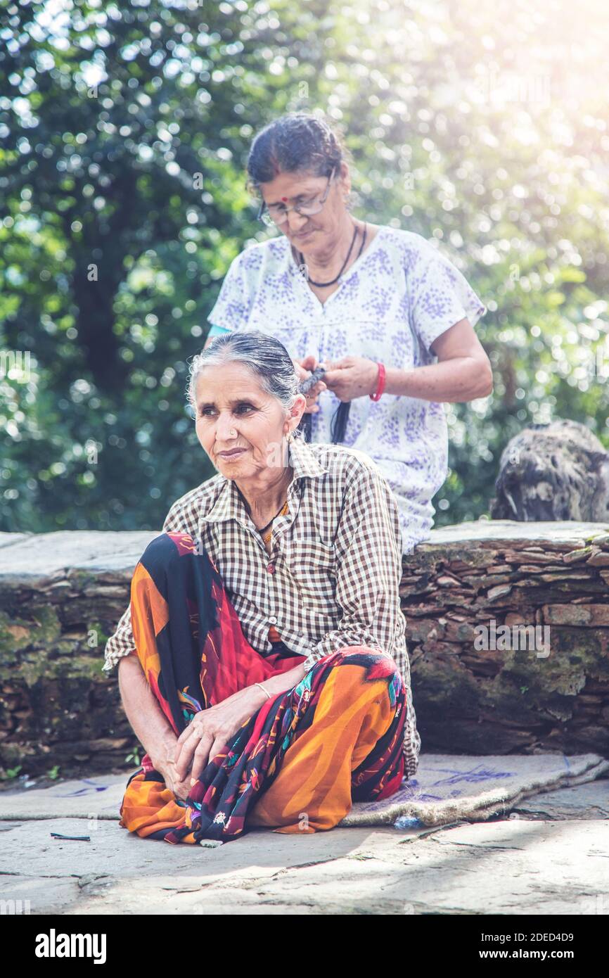 Junge ländliche indische Dorffrau, die ihre Haare von ihrer Schwägerin geflochten hat und Außenseiter ihres ländlichen Dorfhauses sitzt Stockfoto