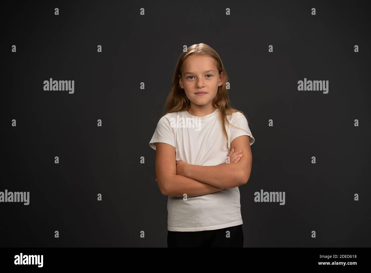 Kleines Mädchen von 8,10 Jahren mit Händen gefaltet sieht aus Fragend an der Kamera trägt weißes T-Shirt isoliert auf Dunkelgrauer oder schwarzer Hintergrund Stockfoto