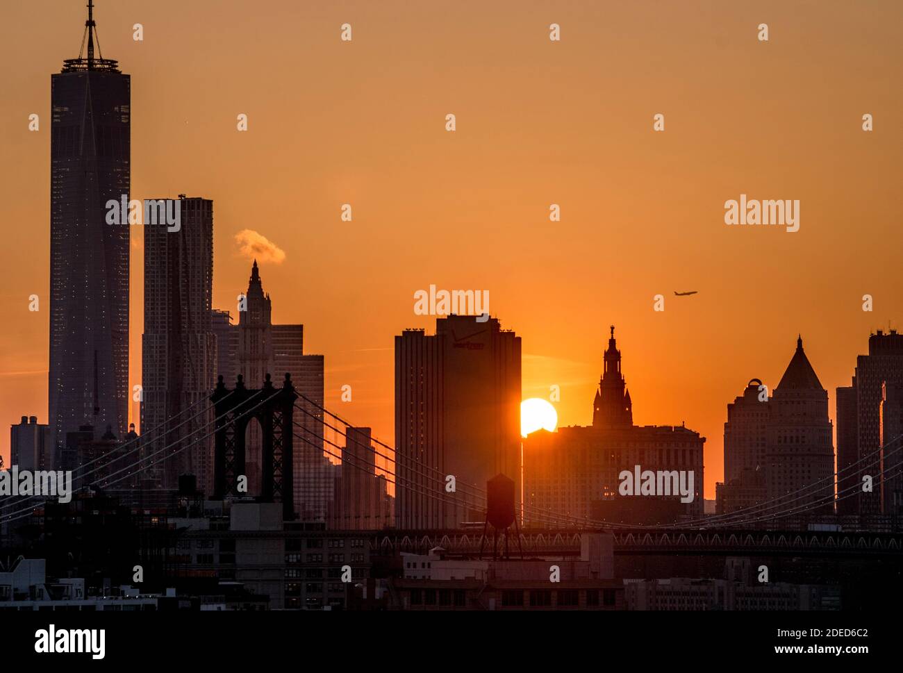 USA, New York City, Manhattan mit dem One World Trade Center ganz links, wenn die Sonne untergeht und ein Flugzeug aufsteigt. Manhattan Bridge im Vordergrund. Stockfoto