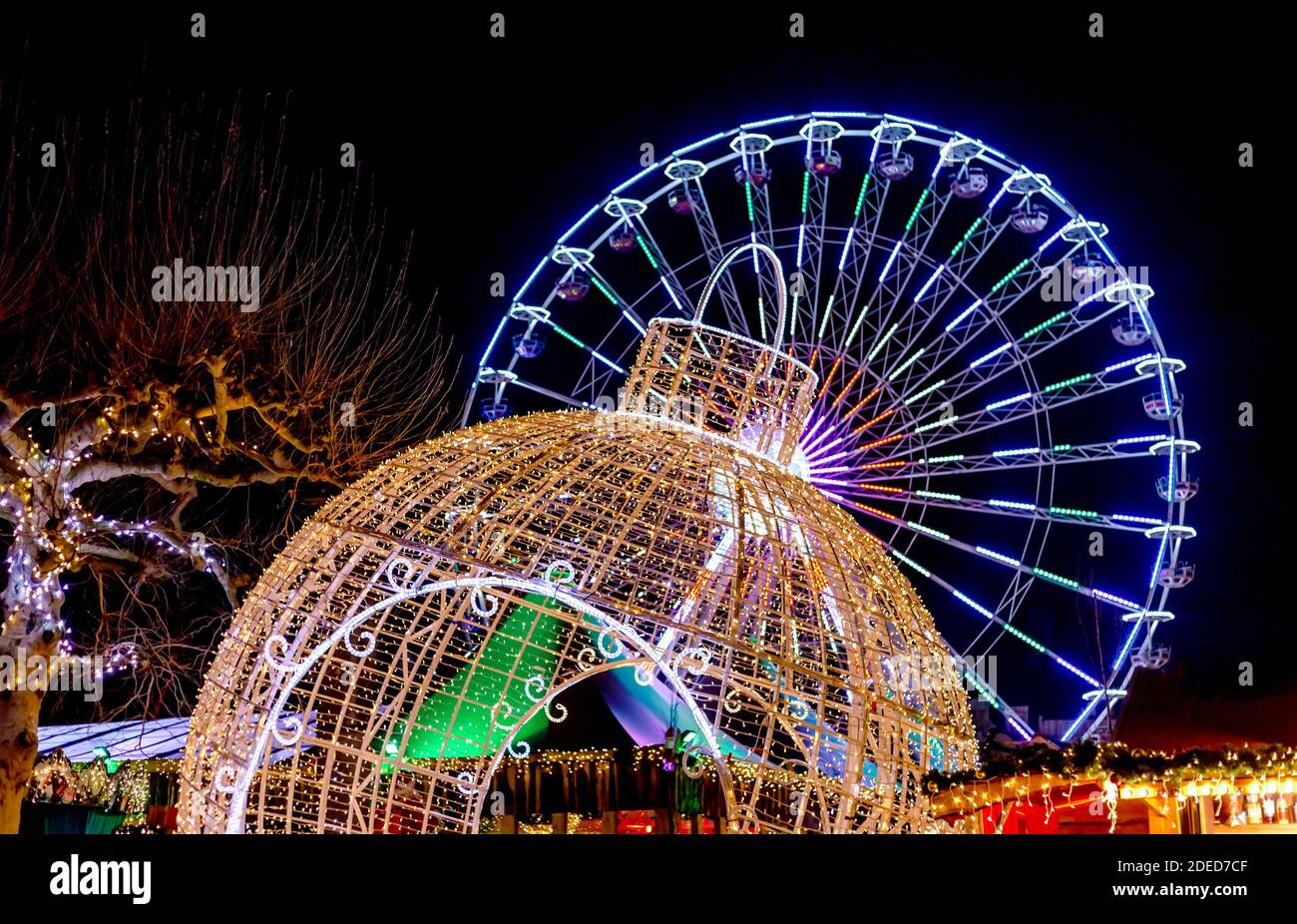 Neujahrsdekoration auf dem Weihnachtsmarkt. Das Riesenrad leuchtet nachts. Riesige Weihnachtskugel und Riesenrad. Weihnachtsmarkt. Stockfoto