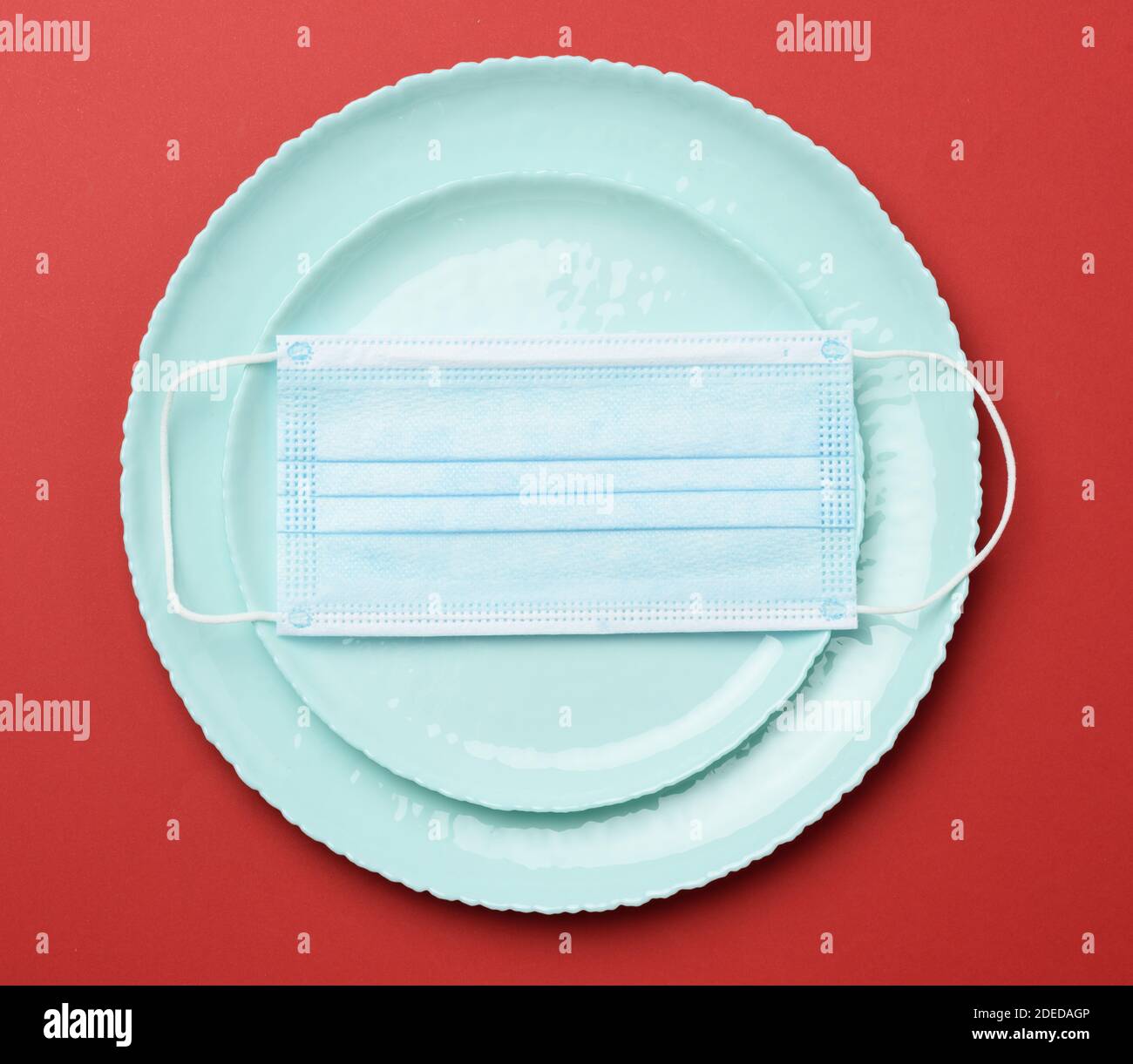 Leere runde grüne d Keramikplatte auf rotem Hintergrund und Einweg-medizinische Maske auf der Oberseite, Restaurant Quarantäne Shutdown Konzept, Draufsicht Stockfoto
