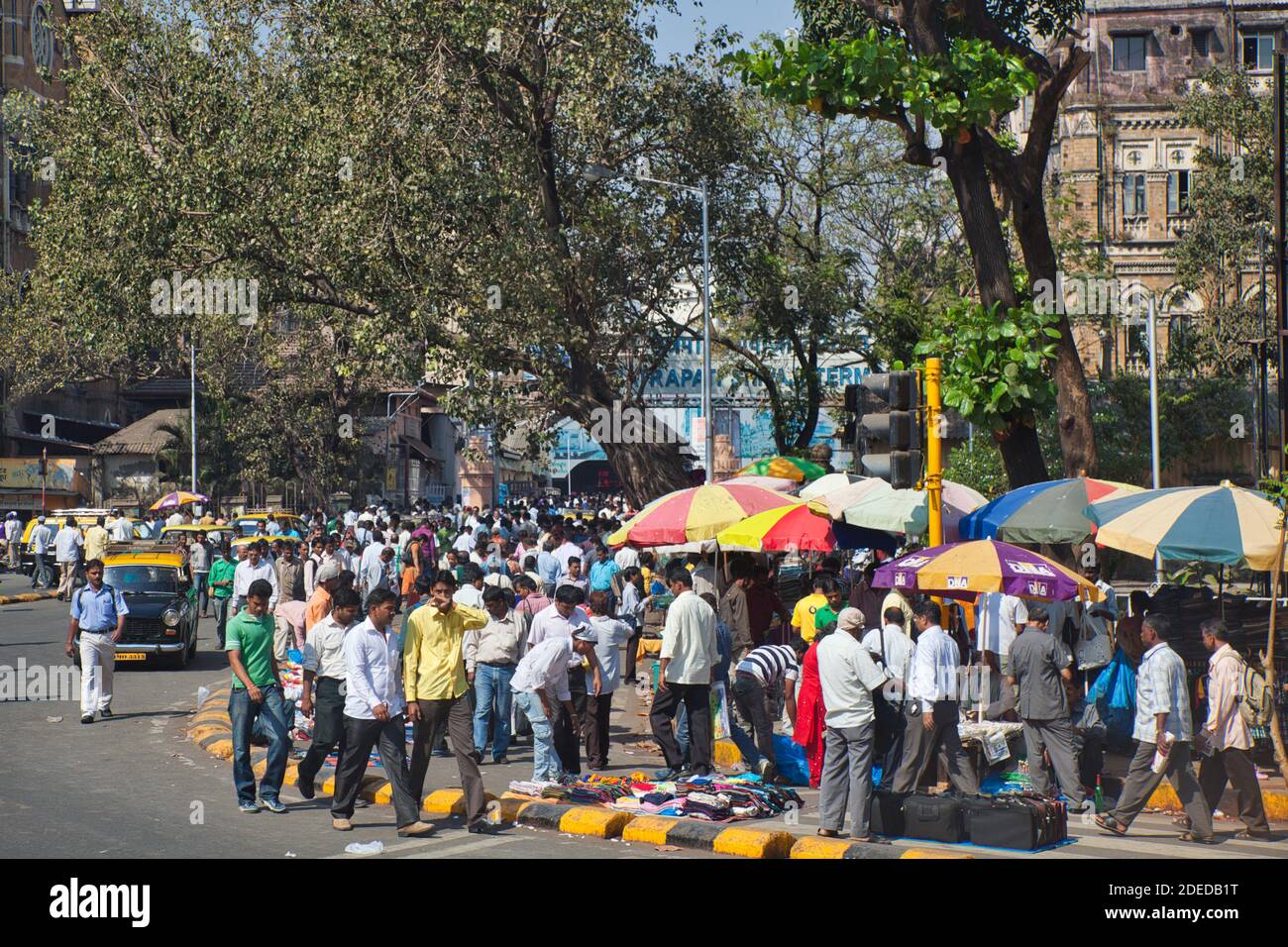 Eine bunte Straßenszene in Mumbai Indien mit Marktständen Und große Menschenmassen plus bunte Sonnenbrollys und Bäume Stockfoto