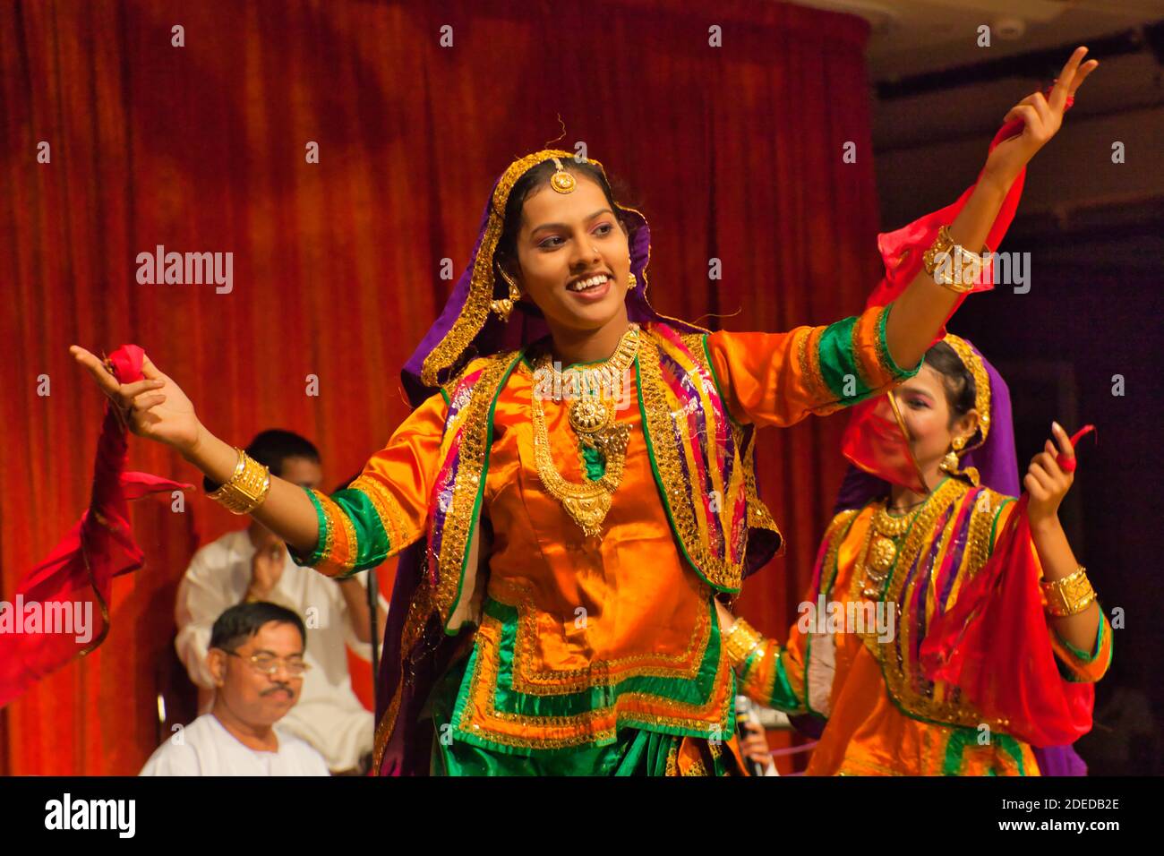 Eine Gruppe von Volkstänzern gibt eine Aufführung in Mumbai, Indien, und eine Tänzerin tritt mit ausgestreckten Armen auf, alles in bunten Kostümen Stockfoto