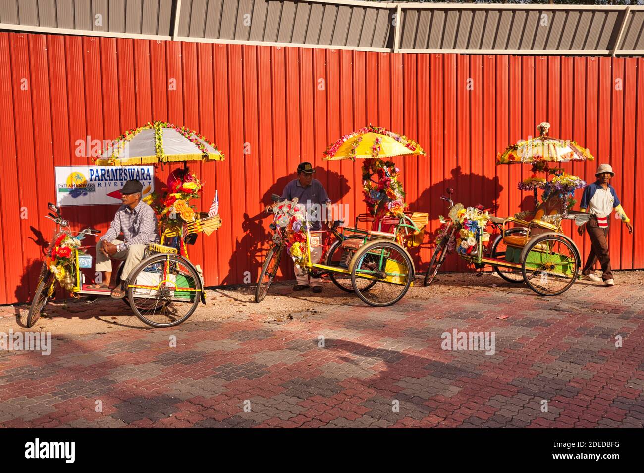 Drei dekorative und bunte Trishaws mit ihren Fahrern erwarten die Kunden auf einer Straße in Malacca, Malaysia Stockfoto