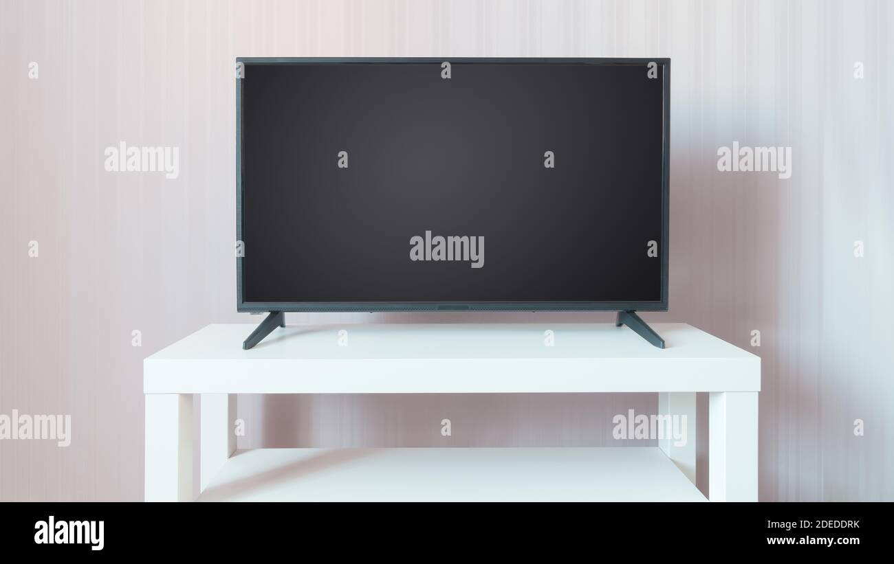 Schwarzer LCD-Fernseher mit leerem Bildschirm auf weißem Ständer vor beigefarbenem Wandhintergrund. Platz auf dem Bildschirm kopieren Stockfoto