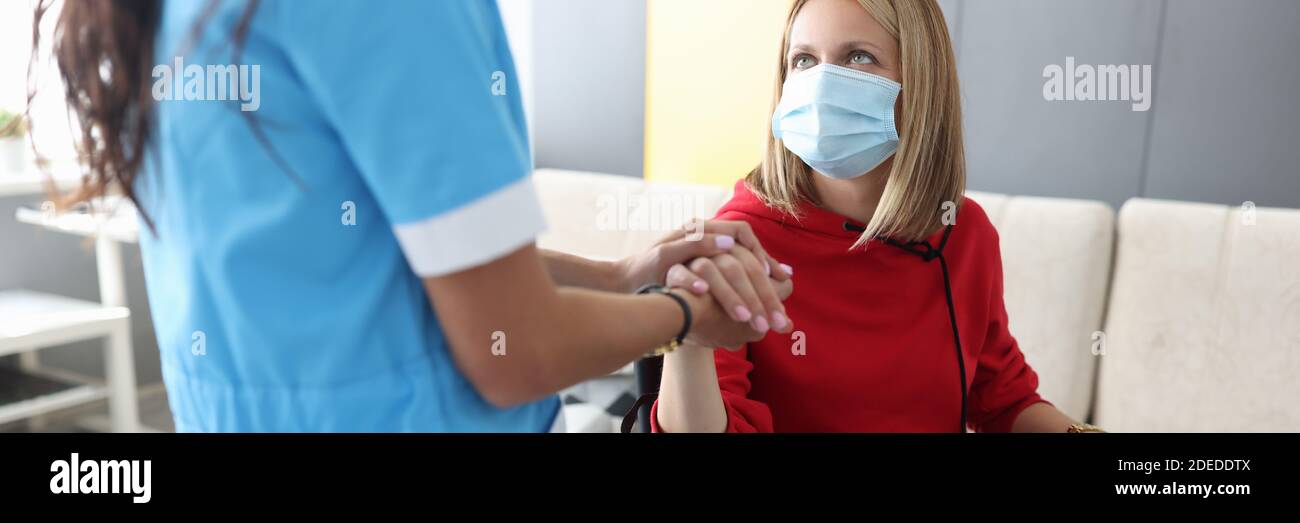 Arzt in Uniform hält die Hand der kranken jungen Frau in Rollstuhlporträt Stockfoto