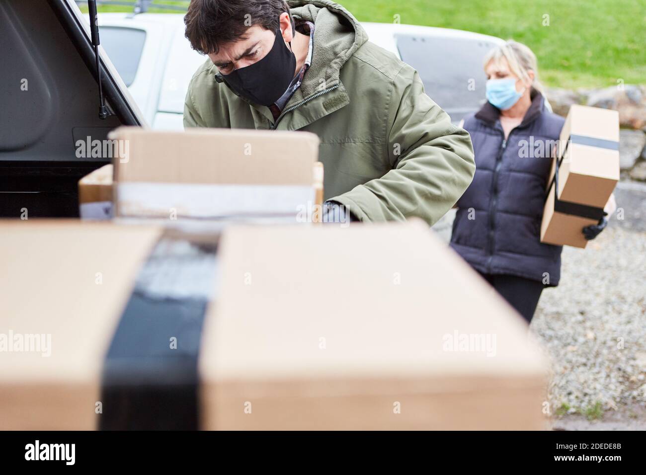 Paketdienst Subunternehmer stapelt Pakete in Auto zu Weihnachten mit Gesichtsmaske wegen Covid-19 Stockfoto