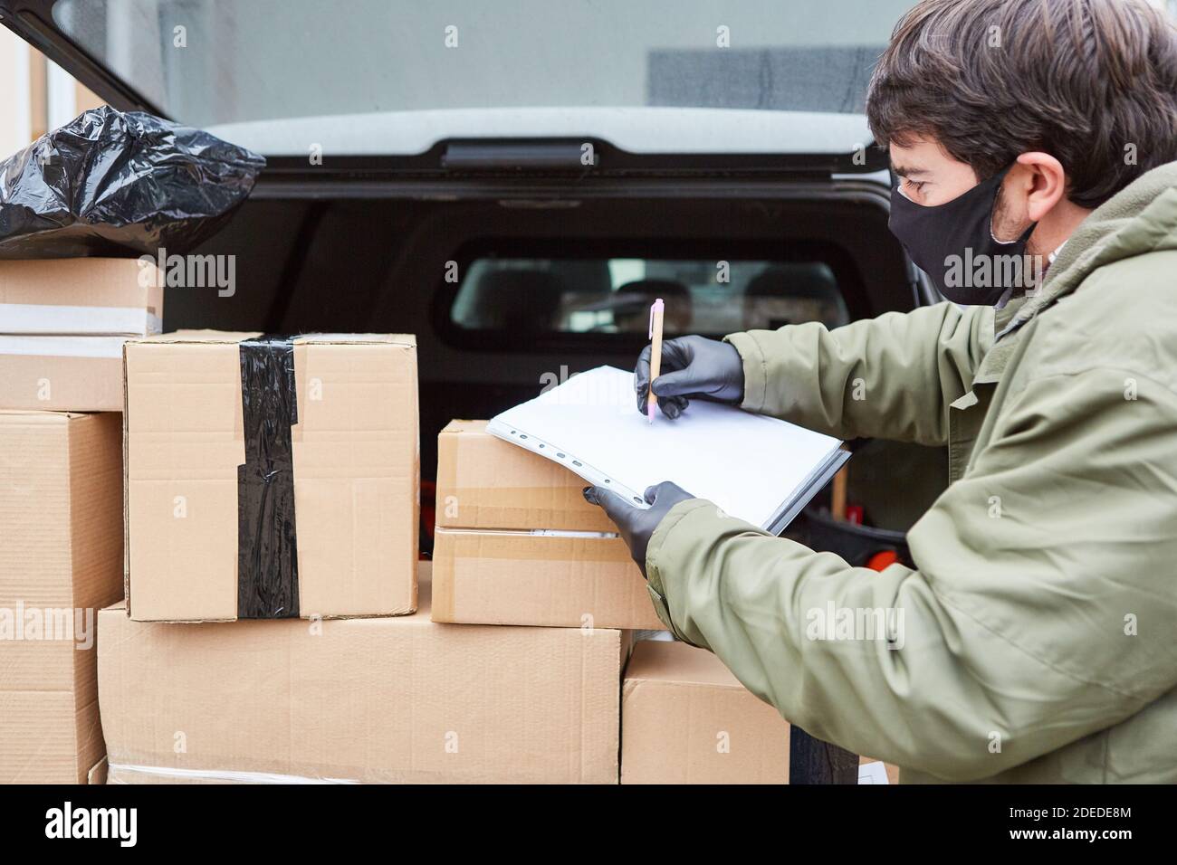 Paketzustellung Mann mit vielen Paketen im Kofferraum von Der Lieferwagen mit Gesichtsmaske wegen Covid-19 Stockfoto