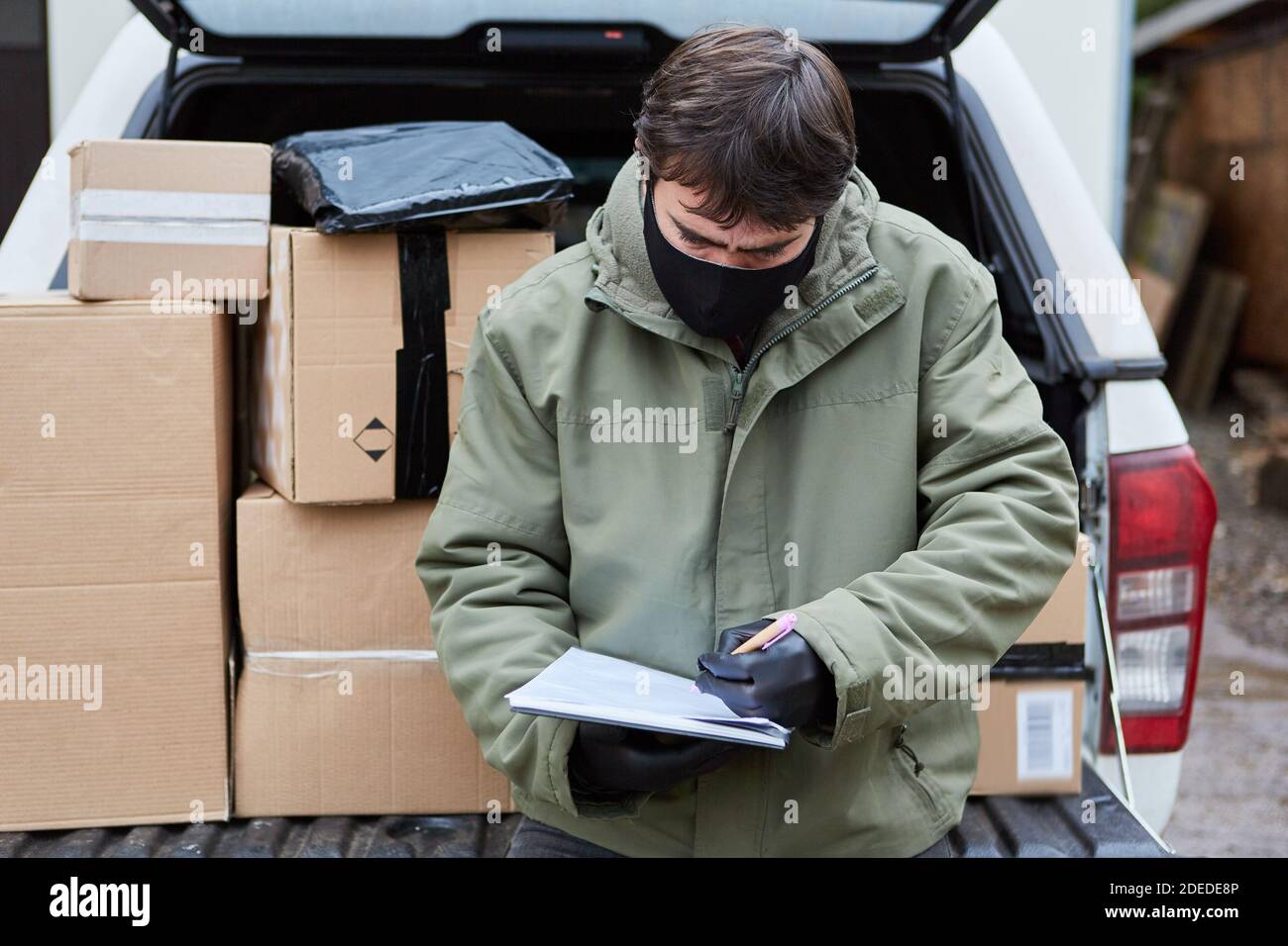 Paketdienst Subunternehmer bringt Pakete in das Auto mit Gesicht Maske wegen Covid-19 für Weihnachten Stockfoto