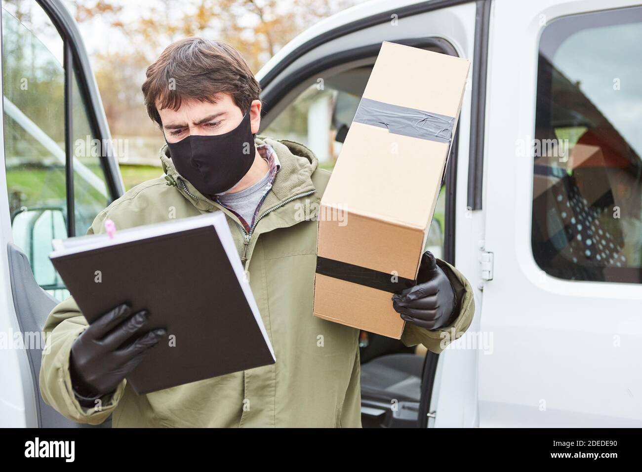 Paketzustellung Mann mit Gesichtsmaske wegen Covid-19 mit Paket sieht Lieferschein für die Lieferung zu Weihnachten Stockfoto