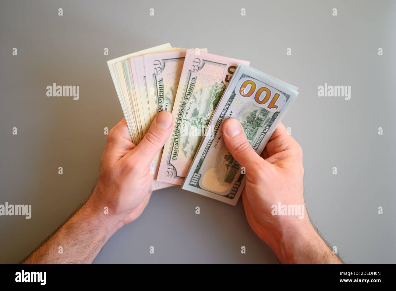 Männer Hände halten und zählen 100 und 50 Dollar Scheine Auf grauem Hintergrund Stockfoto