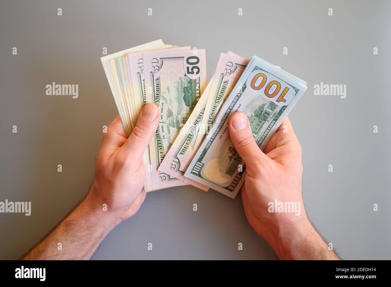 Männer Hände halten und zählen 100 und 50 Dollar Scheine Auf grauem Hintergrund Stockfoto