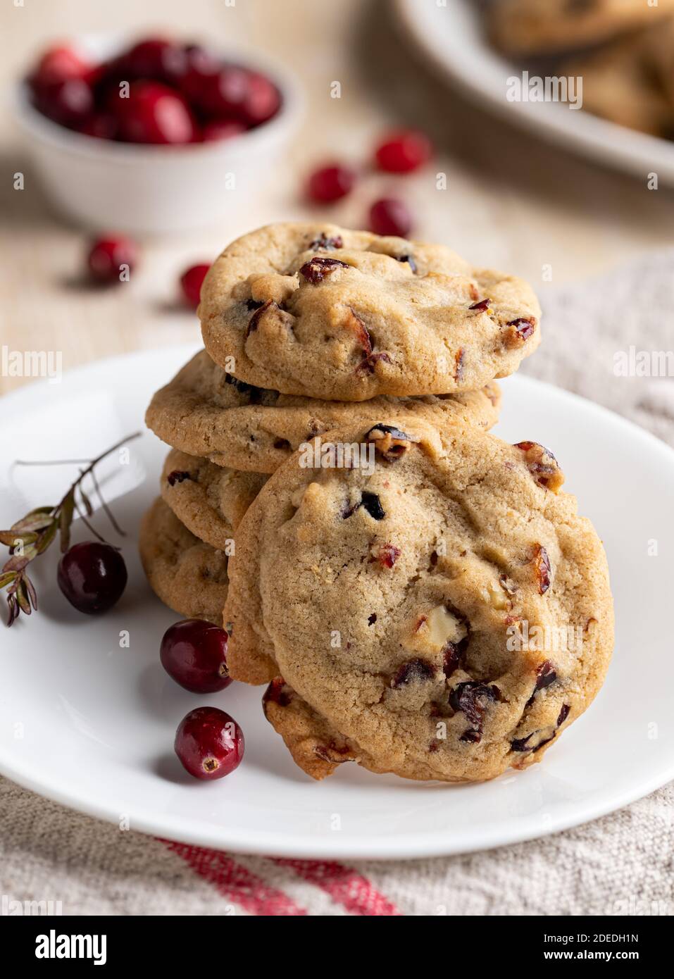Stapel Cranberry Walnuss Cookies auf einem Teller mit Schüssel Von Preiselbeeren im Hintergrund Stockfoto
