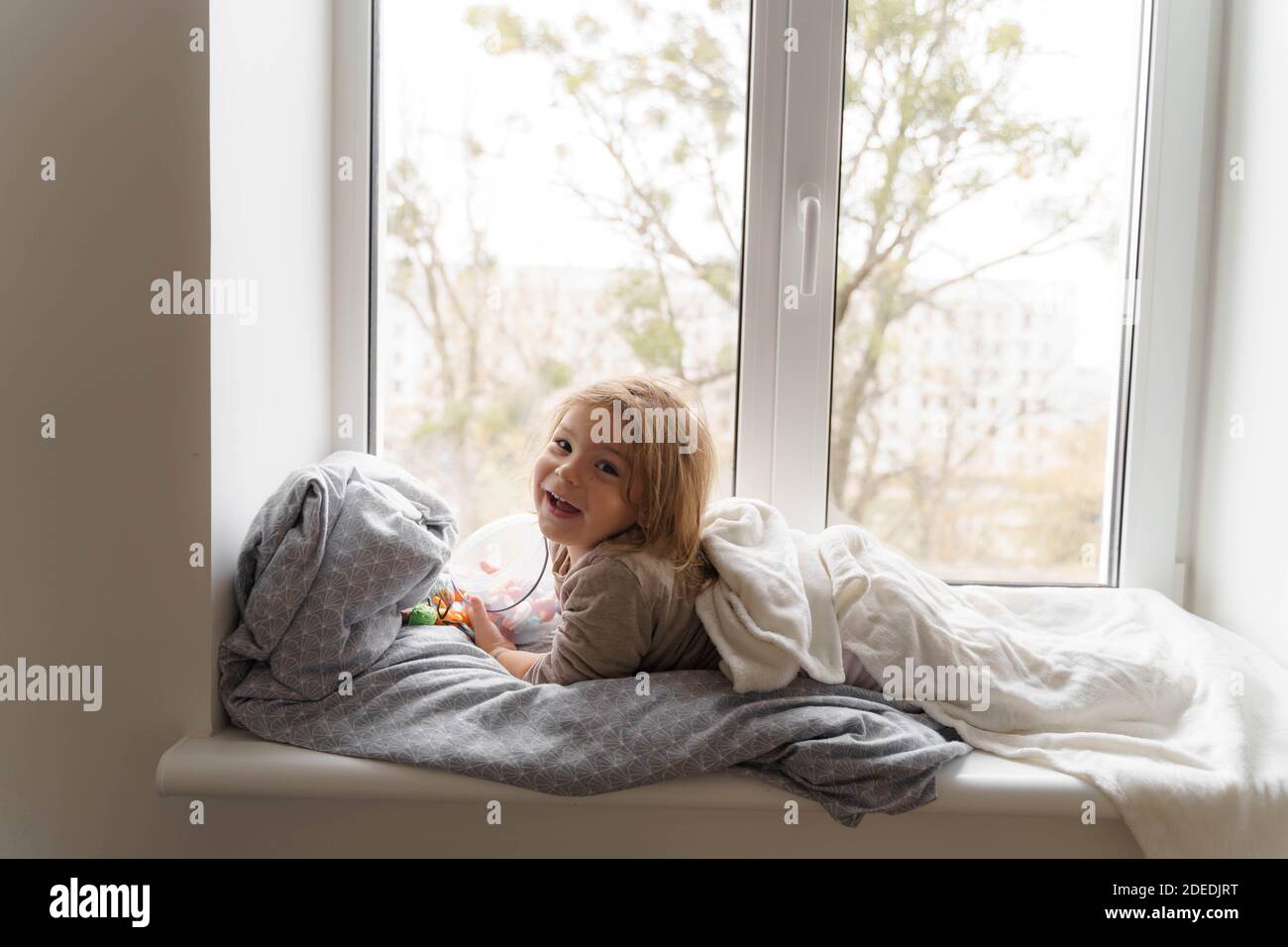 Kind liegt am Fenster im Wohnzimmer und beobachten auf der Straße. Gemütliches Zuhause an Wochenenden, Feiertagen und Absperrung Stockfoto