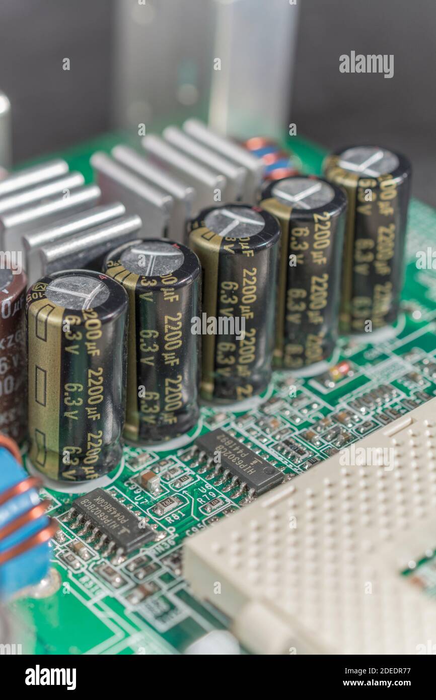 Nahaufnahme einer Reihe von 5 elektrischen Aluminium-Elektrolytkondensatoren auf einer grünen gedruckten Computer-Hauptplatine (pcb). Kühlrippen aus Aluminium. Stockfoto