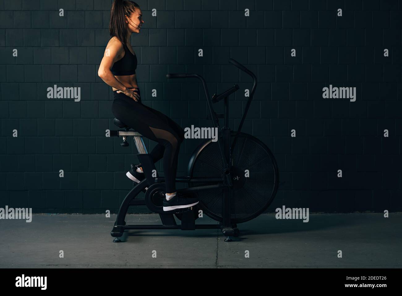 Seitenansicht einer Sportlerin, die auf dem Air Bike sitzt An der Wand und in Ruhe während des Trainings Stockfoto