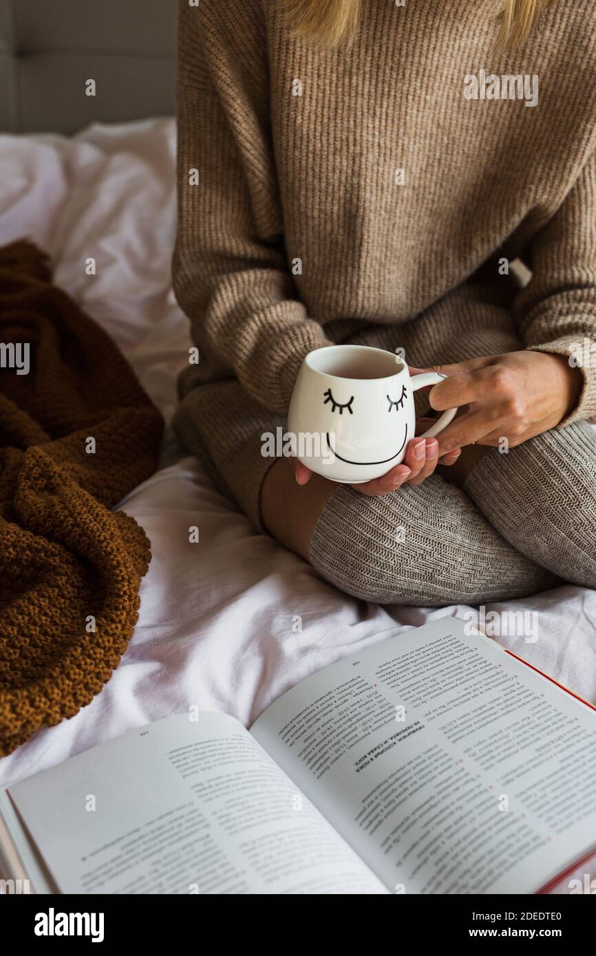 Faule Zeit im Bett. Junge kaukasische Frau mit blonden Haaren 30 Jahre alt Buch lesen und trinken Kaffee oder Tee. Bleiben Sie zu Hause während Coronavirus covid-19 Stockfoto