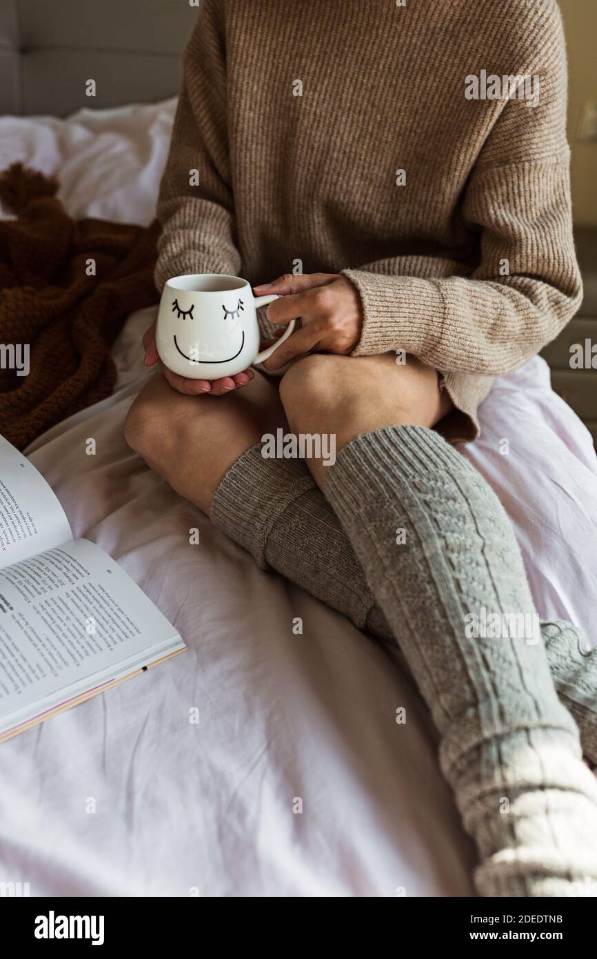 Faule Zeit im Bett. Junge kaukasische Frau mit blonden Haaren 30 Jahre alt Buch lesen und trinken Kaffee oder Tee. Bleiben Sie zu Hause während Coronavirus covid-19 Stockfoto
