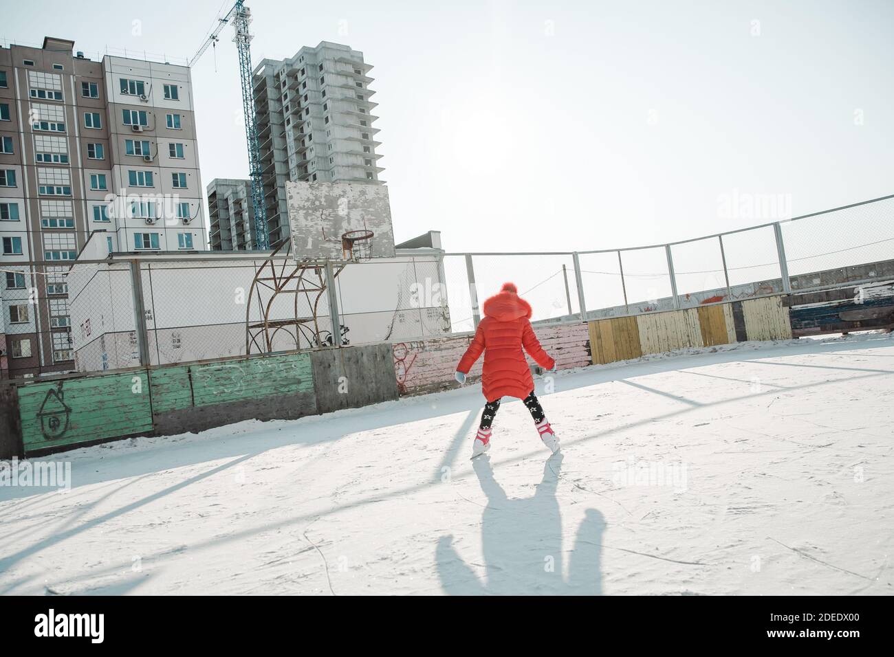 Mädchen in roten Kleidern Skaten in Schlittschuhen auf dem Hof Schlittschuhbahn am sonnigen Wintertag Stockfoto