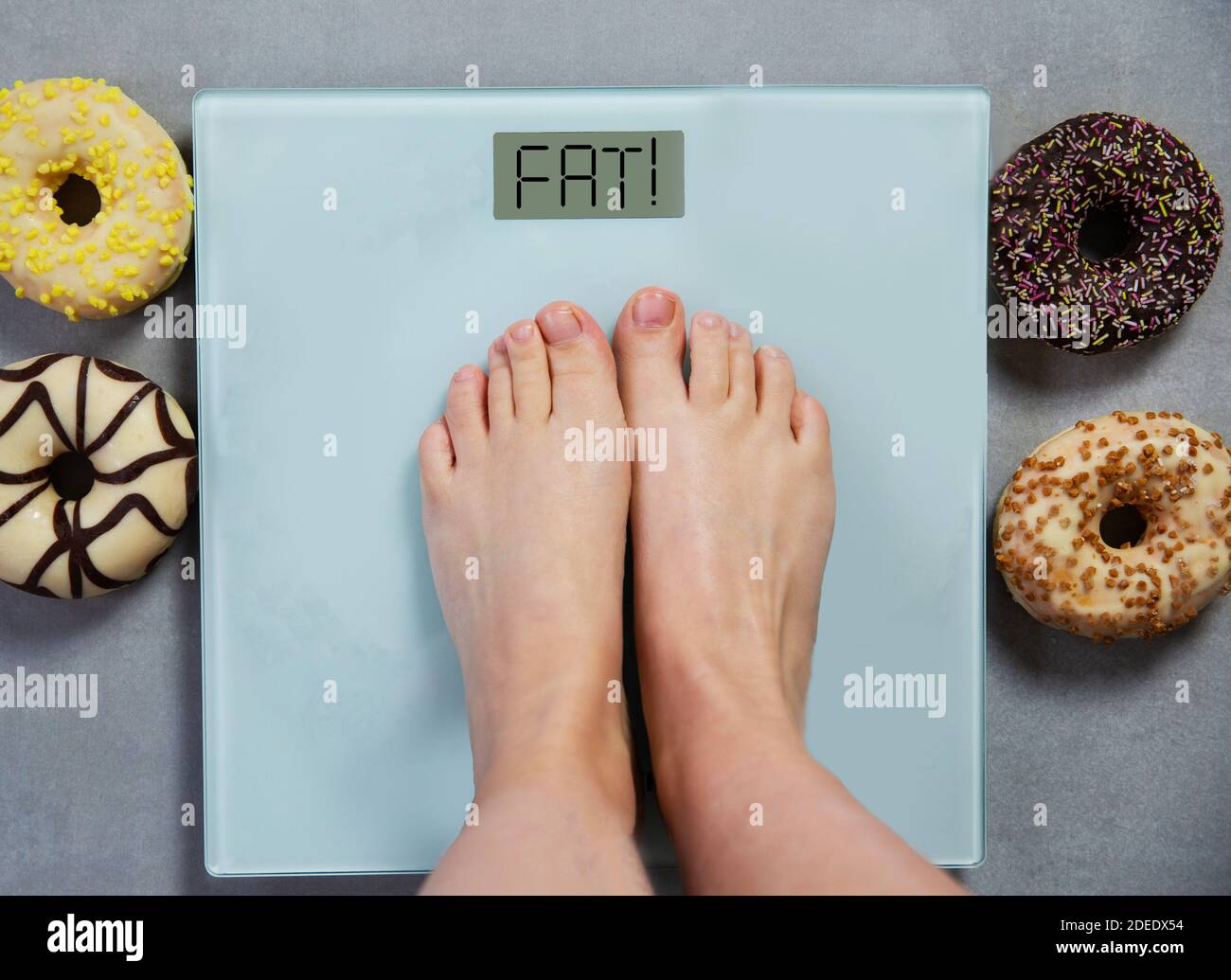 Person steht auf der digitalen Waage mit den Worten FETT und Junk-Food-Donuts auf dem Hintergrund, Diät-Konzept Stockfoto