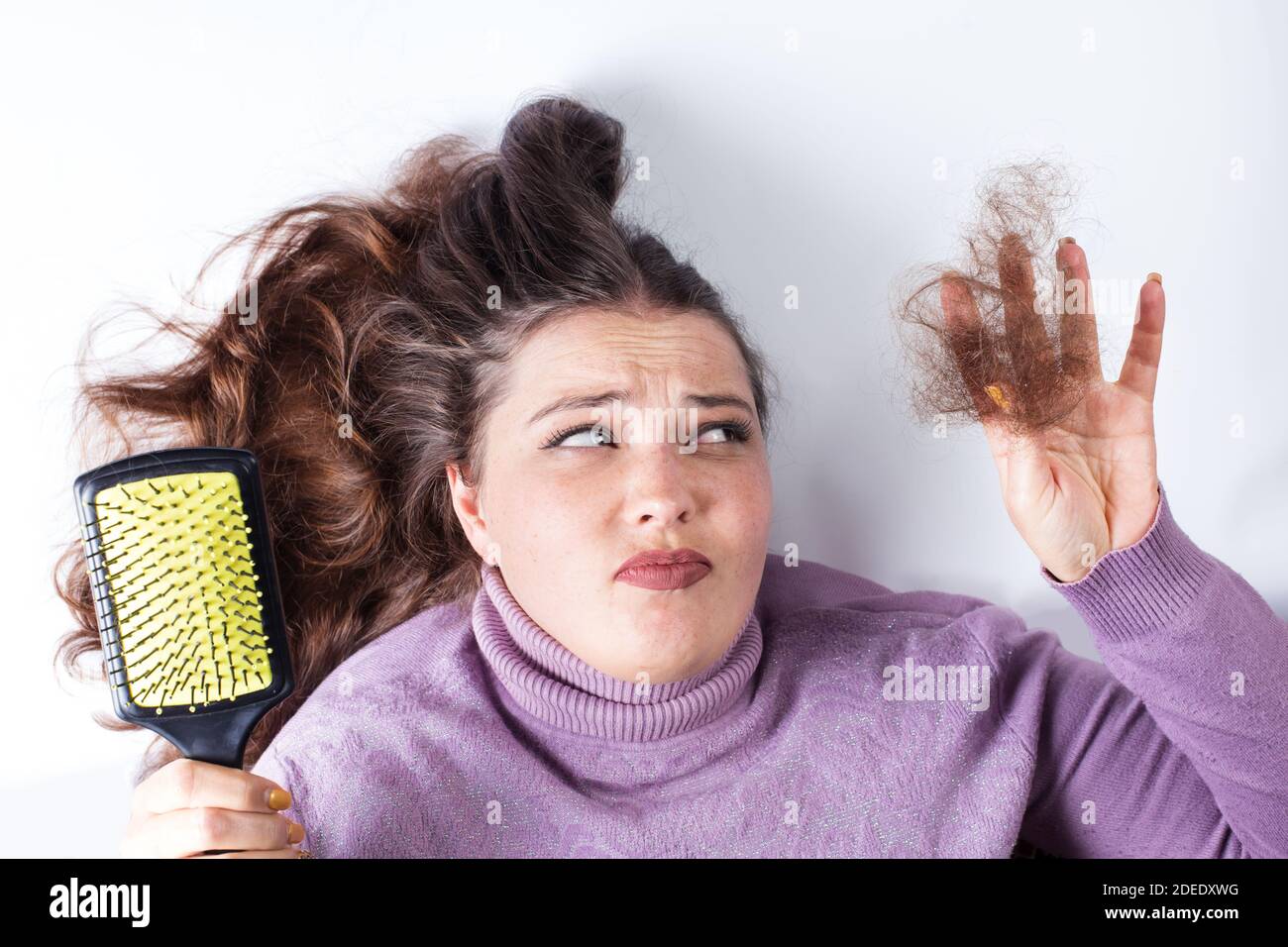 Trauriges junges Mädchen, das lockere Haare in der Hand hält, auf weißem Hintergrund. Stockfoto