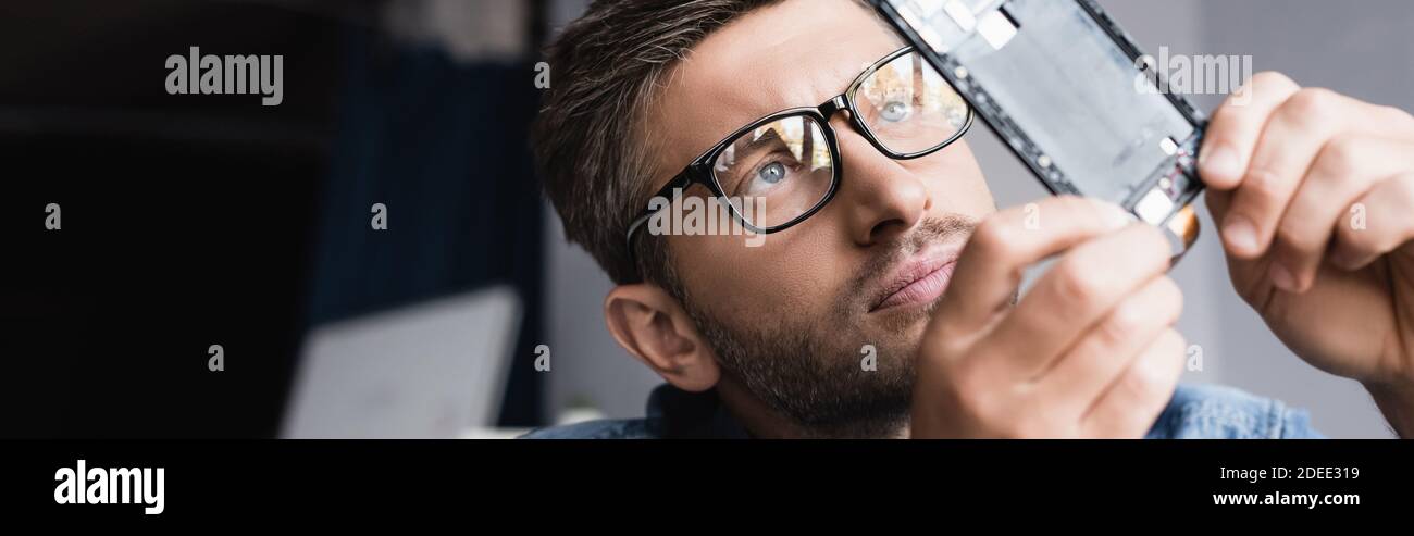 Fokussierte Werkstatt in Brillen Blick auf zerlegten Teil des defekten Handys auf verschwommenem Hintergrund, Banner Stockfoto