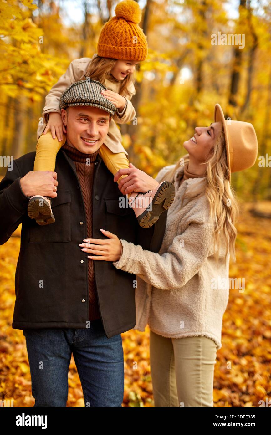 Eltern und Kind gehen an einem sonnigen Herbsttag im Wald spazieren, posieren, lächeln und lachen, tragen warme Kleidung für kalte Tage Stockfoto