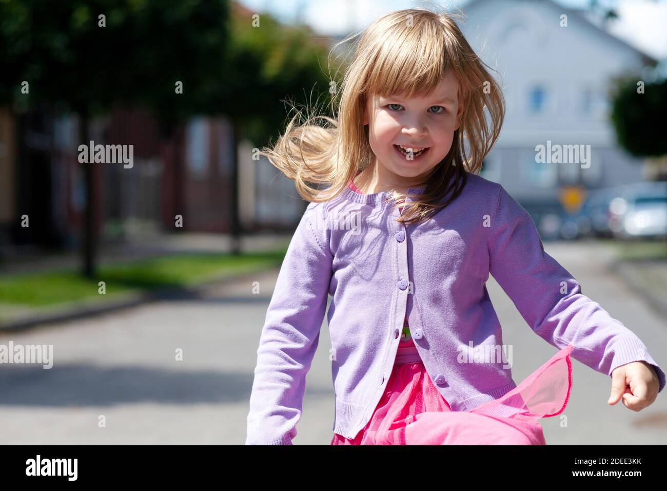 Glückliches kleines Kind läuft auf die Kamera springen. Lächelnd fröhlich aktives Mädchen mit zerstreut fliegenden Haaren schnell in Richtung der Kamera, Nahaufnahme Stockfoto