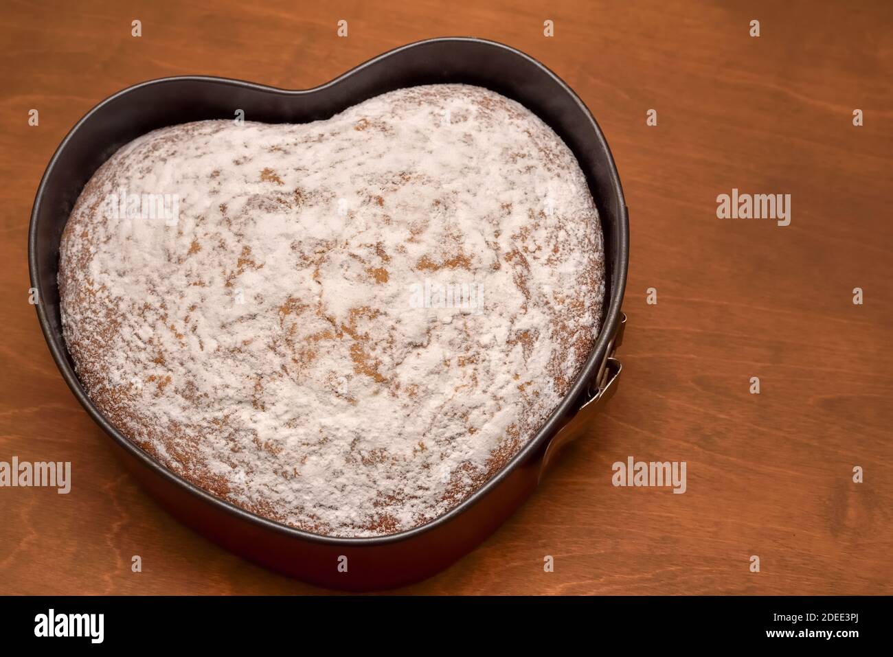 Hausgemachter herzförmiger Kuchen, frisch gebacken und mit Puderzucker bestäubt Stockfoto