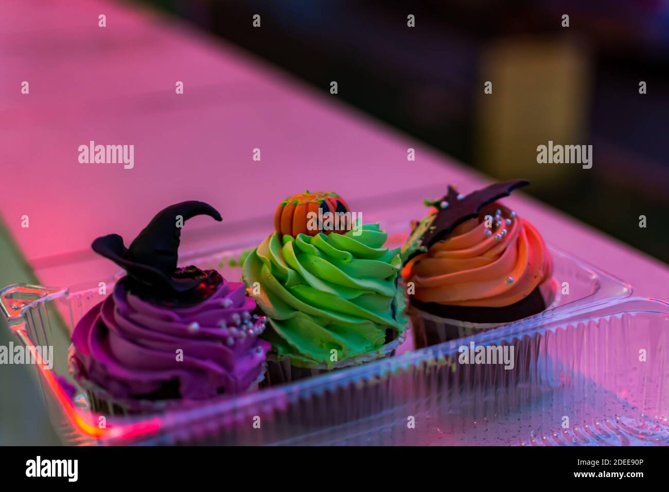 Bunte Kuchen für Halloween. Set von Geburtstagskuchen in einer Plastikbox in Neonbeleuchtung. Schöner Kürbis, Hexe und Fledermauskuchen. Sanfte Abendbeleuchtung. H Stockfoto