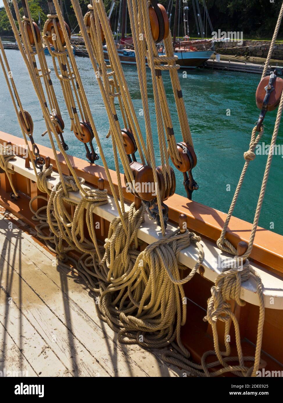 Nahaufnahme von Seilen und Takelage auf einem Segelschiff mit dem Holzdeck im Vordergrund sichtbar. Stockfoto