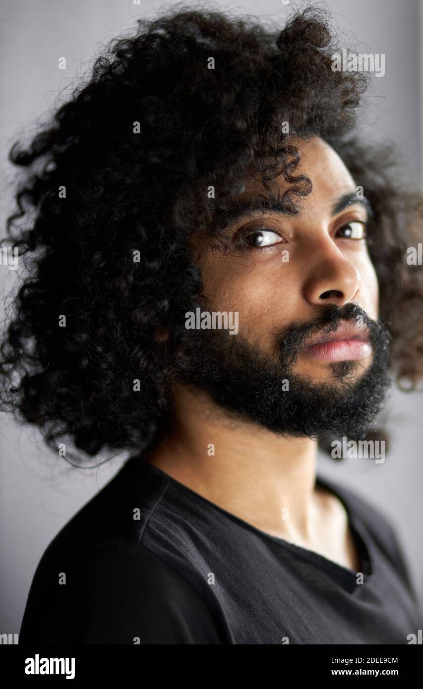 Nahaufnahme Porträt von lockigen indischen Mann mit tiefen Blick, gutaussehende Kerl in lässigen schwarzen T-Shirt ist in der Kontemplation Stockfoto