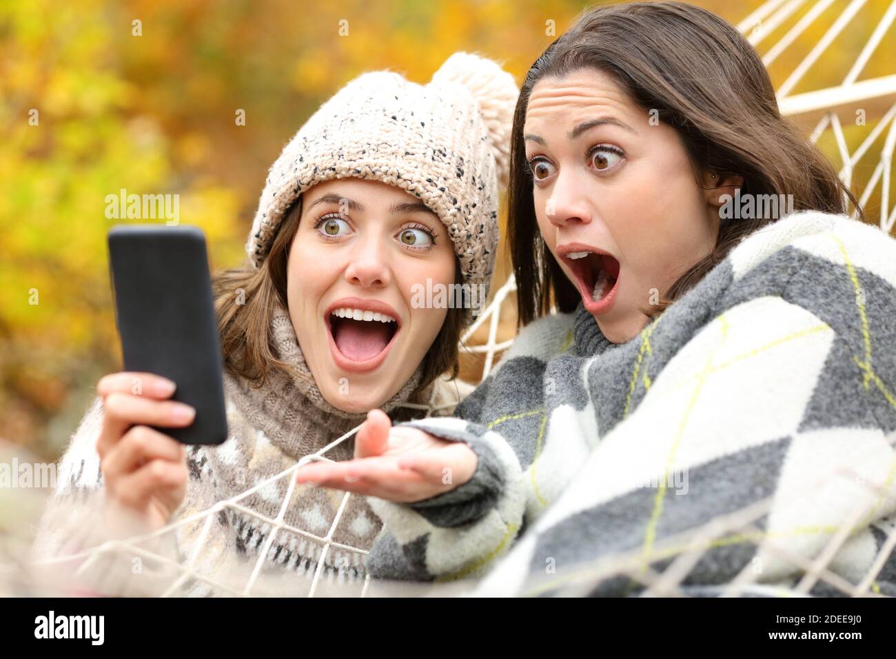 Zwei überraschte Freunde überprüfen gemeinsam Smartphone-Inhalte im Herbst Urlaub Stockfoto